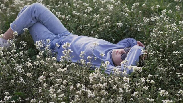 Teenage girl relaxing in the countryside on a sunny day stretched out on the white flowers dreaming in spring-summer season.