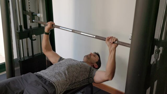 Athletic middle-aged Caucasian man trains bench press for the chest on a sports simulator. training apparatus