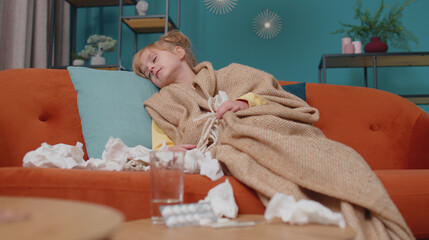 Portrait of one Caucasian child girl in plaid suffering from cold fever or allergy lying on sofa in...