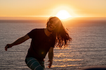 Young man with long black hair at the beach during sunset