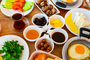 Various foods in Turkish halal breakfast traditions including fried egg, several kinds of cheese, bread, vegetables, olives, sauces and walnuts served on table.