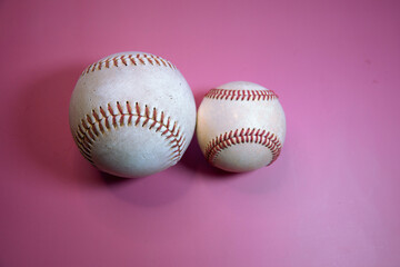 Softball next to a Baseball with a pink background.