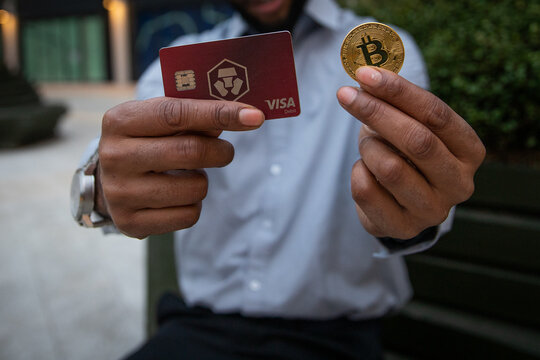 A man holds a Bitcoin coin and the card of Crypto.com, a very popular Cryptocurrency exchange