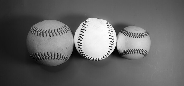Three balls in a row, two softballs, and one baseball.  Black and white photo from the middle ball glowing. 