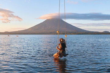 Back view of woman sitting on a swing overlooking the volcano concenpcion on ometepe island,...