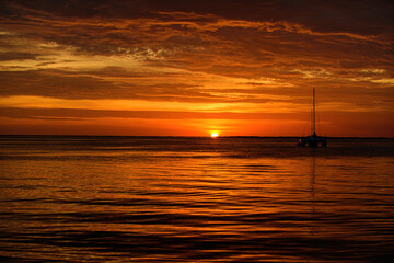 Naklejka na ściany i meble Boat on the sea at sunset. Sailboats with sails. Ocean yacht sailing along water.