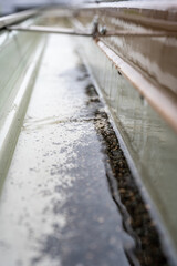 Obraz premium Selective focus on a section of residential guttering with hanger conveying water during a storm. Rain splatters and drops visible.