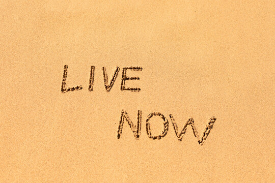 Live now concept written in the sand