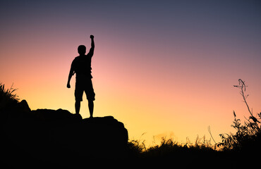 silhouette of a person on the top of mountain with fist in the air. Winning , goal setting, and courage concept. 