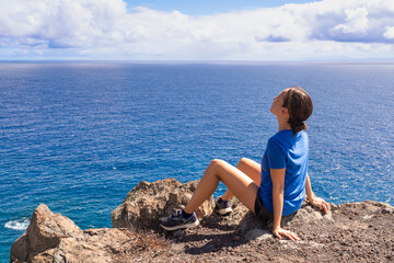 woman sitting on the rocks looking out to the ocean view 