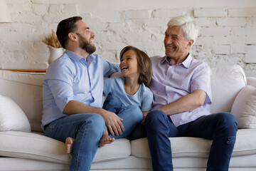 Happy multi generational men sit on sofa in living room, laughing, spend time together at home....