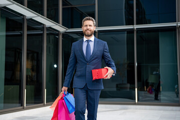 handsome entrepreneur in suit with shopping bags gifts walk outside the office, anniversary.