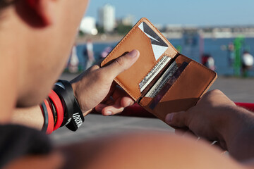 A man on the street is holding an open small comfortable red leather wallet with dollar bills and plastic cards. Horizontal orientation, copy space, close-up, no face, blurred background - obrazy, fototapety, plakaty