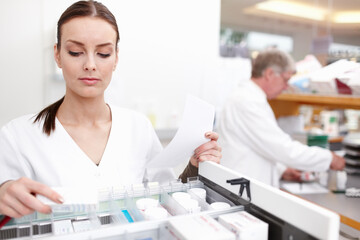 Obraz premium Pharmacist checking medicines with colleague. Portrait of female pharmacist checking medicines with colleague working in background.
