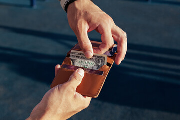 A man on the street is holding an open small comfortable red leather wallet with dollar bills and plastic cards. Blue background, horizontal orientation, copy space, close-up, no face - obrazy, fototapety, plakaty
