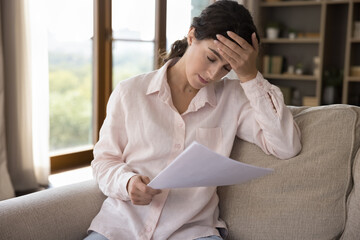 Unhappy frustrated millennial Hispanic woman feeling stressed reading bank loan rejection notice,...
