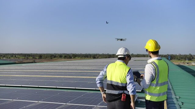 Professional engineer using drone and digital tablet maintaining solar cell panels together on building rooftop. Technician working on ecological solar farm. Renewable clean energy technology concept