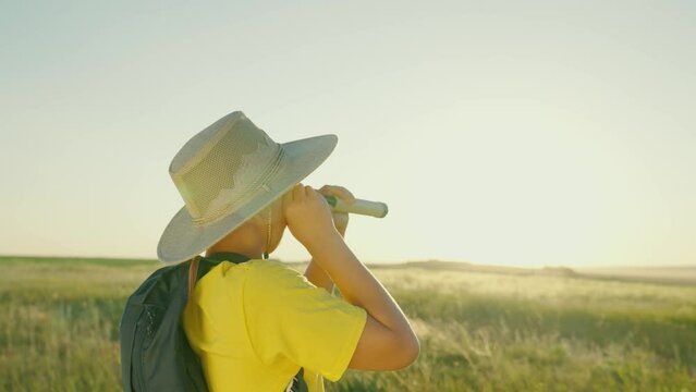 Child boy plays on the field as a traveler. Son in a summer park in a hat looks through a spyglass, childhood dreams. Children's dreams, scientist discoverer, children's fantasies, adventures, travel