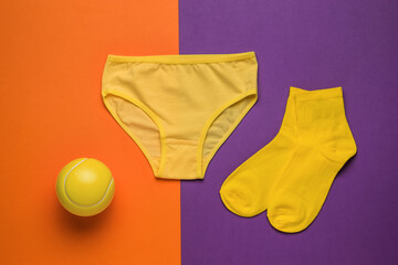 A set of yellow ball, socks and panties on a purple and orange background.