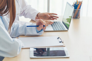 Two asian women doctors discuss meeting doctor's office medical clinic using laptop consulting...
