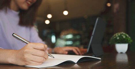 Closeup image of woman using pen writing on notebook or paper report in office.