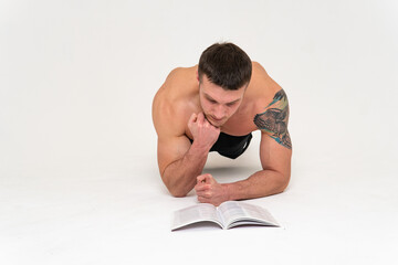 Fototapeta na wymiar Bodybuilder reads the book on a white background isolated at the bottom of his head on his hands man young reading, athletic bodybuilding muscles, Isolated gym, posing tan