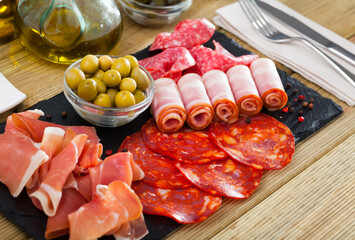 Slices of Spanish dry-cured gammon, chorizo, salami and bacon served with green olives on slate board..