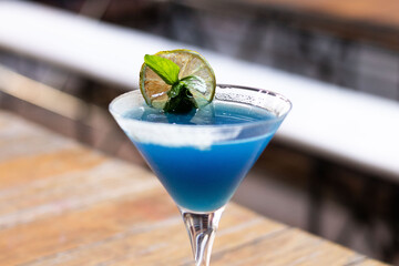 Bebida azul en copa de martini con menta y limón deshidratado 