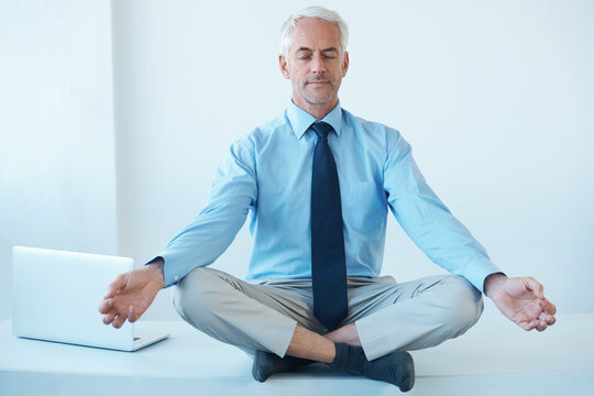 Finding his center. Full length shot of a mature businessman sitting cross legged and meditating.