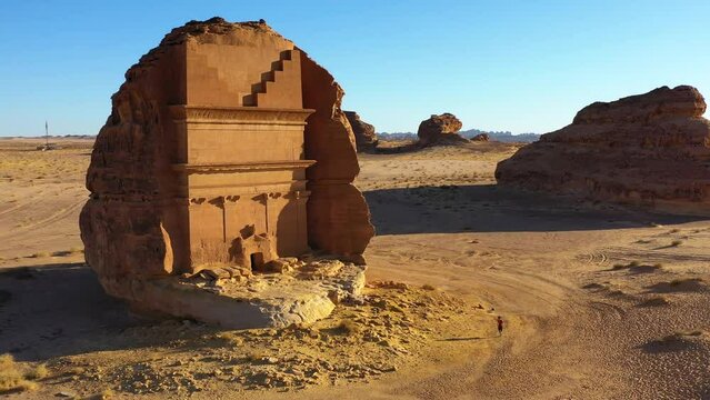 Aerial view of a man running in front of the Hegra in Mada'in Salih, Saudi Arabia - rising, reverse, drone shot