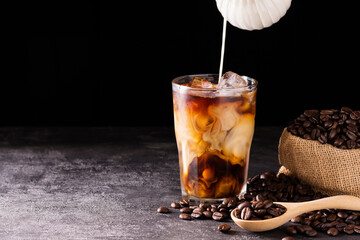 Iced coffee latte in a glass with milk or cream With roasted coffee beans laid out on a wooden...