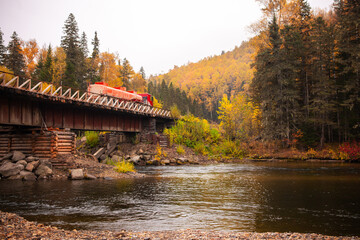 Red fuel truck at wooden bridge over mountain river in autumn