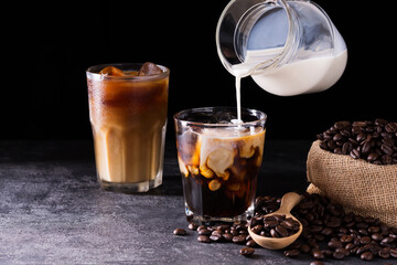Coffee, iced latte in a glass with milk or cream On a wooden table at a coffee shop on a dark black background