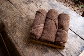 Fototapeta na wymiar Three brown towels folded into a cylinder are placed on a wooden table. prepared for customers to wipe yourself in a resort in the middle of the forest
