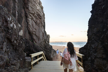 Mujer latina. Señora de espaldas, caminando sobre una pasarela peatonal entre las grutas. Parque natural de Punta del Este. - obrazy, fototapety, plakaty