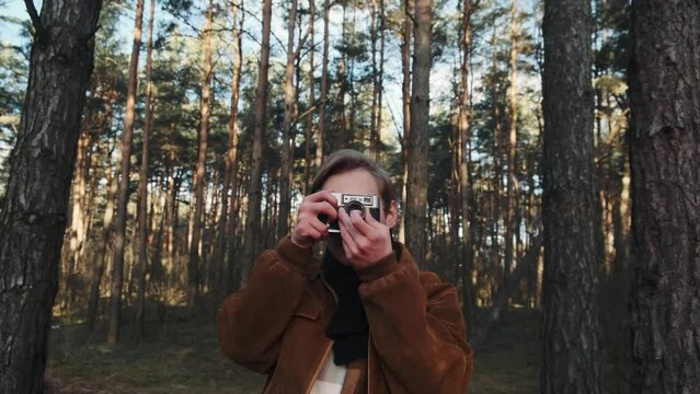 A young blond male photographer takes pictures of nature. Photographer takes pictures in the woods with a retro camera. Young photographer dressed in retro style. . High quality 4k footage