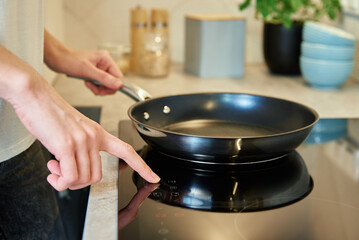 Woman turn on button on induction stove with steel frying pan in the kitchen, Modern kitchen...