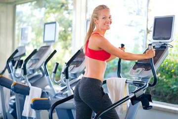 Fototapeta premium Working on her fine form. Shot of a beautiful young woman working out on a stepping machine.