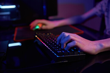 Teenaeger boy play computer video game in dark room, use neon colored rgb mechanical keyboard,...