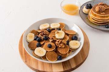 Trend food - mini pancakes with berries and banana slices in a bowl on a wooden round board. delicious breakfast.
