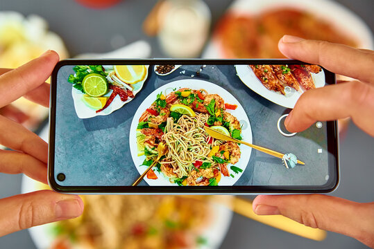 Woman take food photo with smartphone for social media, phone camera taking photo of stir fry wok noodle with shrimps