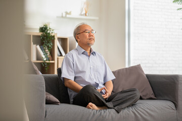 Mature Asian man doing yoga for meditation on yoga mat in living room at home.Clam of senior or elderly men meditation deep breath and relax at cozy home.Happy Retired Meditation at home concept - obrazy, fototapety, plakaty