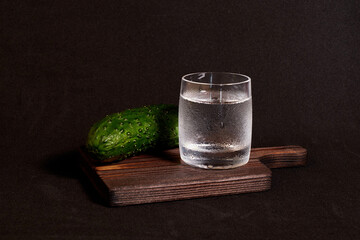 A glass of vodka and a fresh cucumber on a wooden stand