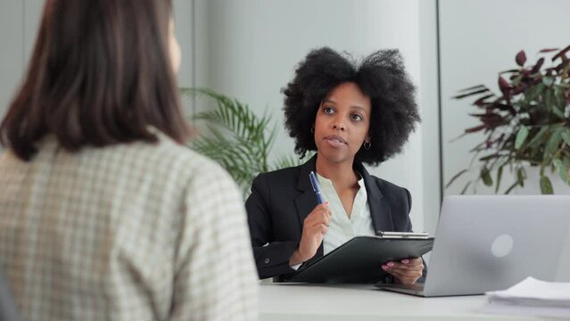 Female employer interviewing job seeker and sitting at table with laptop in company spbi. 4k video Closeup view of beautiful businesswoman talks to female candidate and reads resume, looks with smile