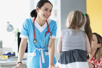 Pretty pediatrician chatting with cute patient child girl on appointment in clinic