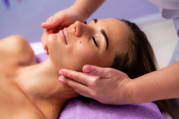 Obraz na płótnie Canvas Relaxing massage. European woman getting facial massage in spa salon, side view