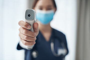 Temperature checks are important during this pandemic. Shot of a young female doctor pointing a thermometer in an office.