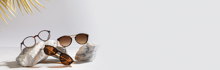 Sunglasses and glasses sale concept. Trendy sunglasses on gray background with golden palm leaves. Trendy Fashion summer accessories. Copy space. Summer sale banner. Optic store discount web line