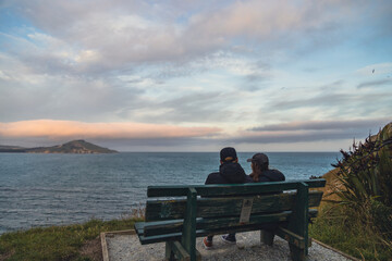 Naklejka na ściany i meble Couple sitting on bench looking at the ocean