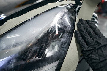 Gloved hand covering headlight edges with adhesive strip